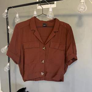 Croppad skjorta med korta ärmar från Monki i en rostbrun färg. Använd 1 gång. Köparen står för frakten🫶🏼