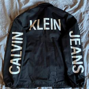 Svart Calvin Klein jacka med text över ärmar och rygg. Knappt använd så den är i mycket bra skick. Storlek S men är oversized så sitter mer som en M.