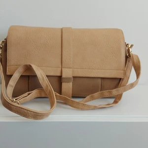 Beige väska - Beige lite större axelremsväska med justerbar och avtagbart band. Fack på utsidan och magnetknapp. Väldigt bra skick. Priset är exklusive fraktavgift.