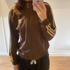 Adidas kofta - Brun och guldig kofta från adidas! Lappen är bortklippt så ser ingen storlek men skulle säga S eller M! Fint skick, nästan aldrig använd. Pris - Högsta budet + frakt! Avslutas torsdag 13:e oktober 18:00:)