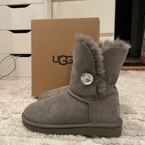 Uggs - Ett par gråa uggs med diamantknapp som detalj på sidan. Fick de för något år sedan men har aldrig kommit till användning.   STORLEK 36  I nyskick!           NYPRIS: 2495