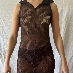 Tajt kort klänning i brun spets med luva. Materialet är tunt och genomskinligt. Använd ett fåtal gånger. 