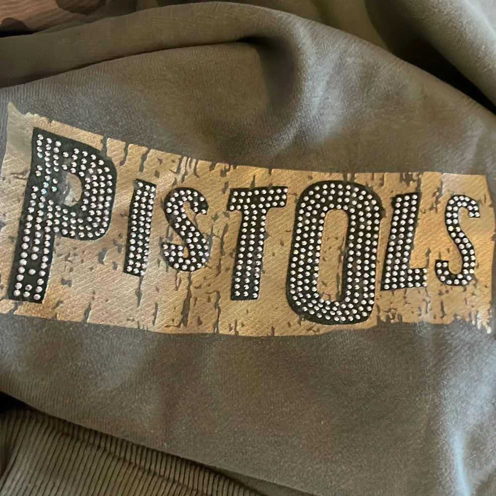 Super fin militär grön hoodie med med rhinestone tryck där det står  Sue’s (framme) pistol (bakom) och jewel på armen. Köpte den på second hand butik lokalt. Hittade ingen användning så jag säljer här på Plick!   Köparen står för frakt!. Hoodies.