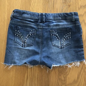 Shorts med glasdetaljer - Blåa jeansshorts med rhinestones. Lappen är avklippt men dem går att justera i midjan. Personligen brukar jag ha XS/S. Skriv om du har frågor eller vill ha fler bilder! Köparen står för frakt. Kan även mötas i Stockholm.