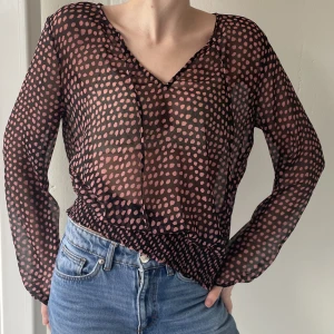 Blus  - Svart med rosa prickar. Transparent med lite balkongärm. Ruynkad och dekorativa ”muddar” och nederkant. 