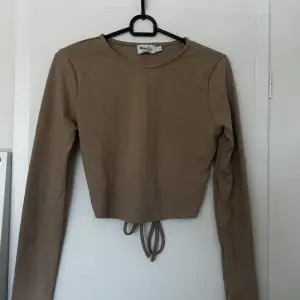 En beige/brun tunn långärmad tröja med en fin knytning i ryggen från NA-KD. Tröjan har aldrig använts. Pris går att diskutera 💕