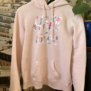 Ljusrosa hoodie från Hollister med text på med blomster motiv.