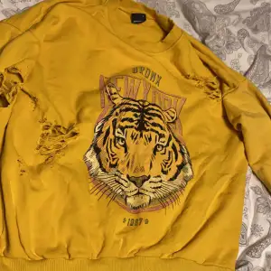 En gul tröja med tryck av en tiger, super fin till våren/hösten, storlek s men passar också folk med medium, kommer från Ginatricot, den är använd en del det kan man se på trycker som är lite urtvättat men det är inga fläckar eller något sånt.🫶🏻