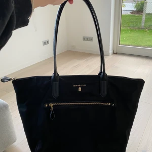 Michael kors väska  - Jättesnygg skolväska/totebag från Michael Kors i mattsvart + gulddetaljer. Finns även äktenhestbevis iform av kod som finns i väskan. Den är som nyskick och själs då den inte kommer till användning. Finns inte att köpa längre därför lite unik🤩☺️ 