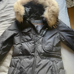 Hollies livigno long black/nature - Vinterjacka från hollies i nyskick. Ser ut som ny, inga skador eller märken. iprincip oanvänd. Äkta pälskrage. Köpt för 5.498kr i storlek 40 på hollies hemsida. Passar även en storlek 38. 