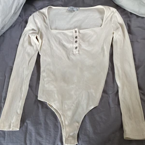 Topp - Vit body med knappar, passformen är lite fyrkantig vid bysten vilket gör att bh bandet kan synas. Den är använd va 2-3 gånger 