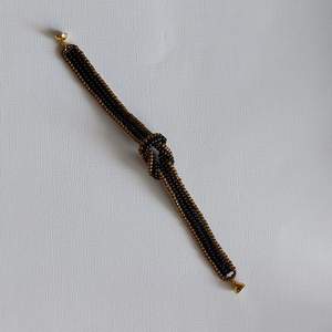 Ett egentillverkat armband av miyuki seed beeds i svart och brons Med en knut på mitten och magnetlås  Armbandet är 12mm brett, knuten 3×2cm Och är 18,5cm långt, mönstret hämtat från Youtube  Frakt 13kr