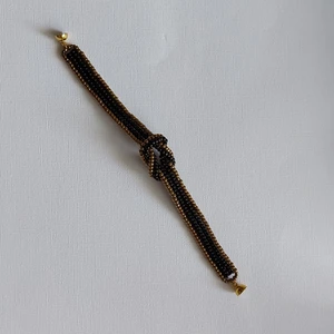 Ett armband av pärlor  - Ett egentillverkat armband av miyuki seed beeds i svart och brons Med en knut på mitten och magnetlås  Armbandet är 12mm brett, knuten 3×2cm Och är 18,5cm långt, mönstret hämtat från Youtube  Frakt 13kr