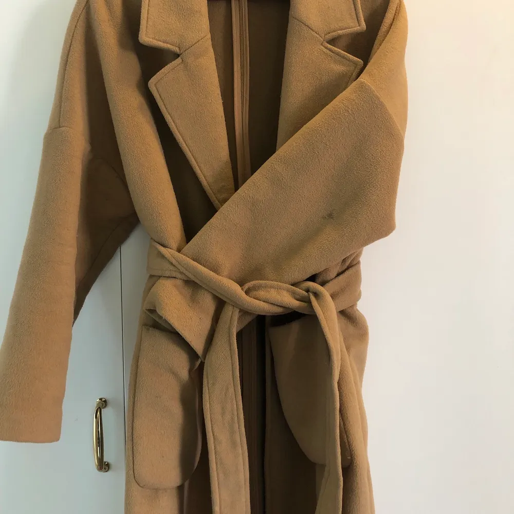 Beige lång kappa från weekday. Använt skick men har mycket kvar att ge. Lite nopprig men enkelt att få bort med tex rakhyvel och en liten fläck på vänsterarmen, syns på sista bilden men inget som märks. Löst skärp att knyta i midjan om man vill!. Takit.