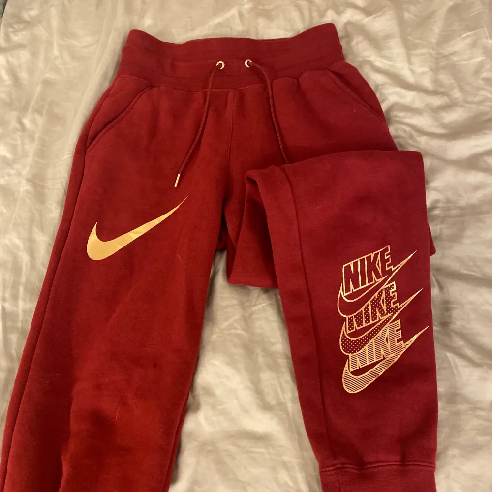 Röda sweatpants ifrån Nike med guld detaljer! Byxorna är i nyskick!. Jeans & Byxor.