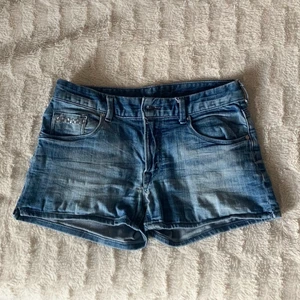 Blå jeansshorts - Säljer ett par gamla jeansshorts som är lågmidjade i storlek 34. Shortsen har detaljer på bakfickorna. Hör av dig för fler bilder eller om du är intresserad! 