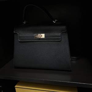 Svarta väska som likar hermes. Svart läder med gulddetaljer.  Följer även med ett axelremsband.  Väskan är ca 28 cm bred.