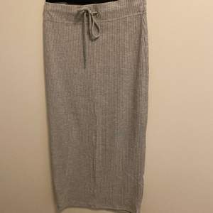 En grå ribbad kjol som är lite längre än till knäna och går att knyta i midjan.