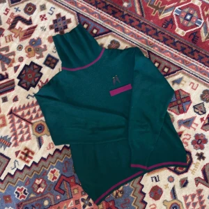 Vintage tröja, mörkgrön st. 36 - Polotröja i härlig mörkgrön färg med vinröd/lila som accentfärg. Perfekt inför jul och vinter! En fake-ficka på framsidan med broderade fåglar. Ribbad nertill och vid ärmslutet. Så mjuk och skön! (Och troligtvis vintage!)  ullblandning. 