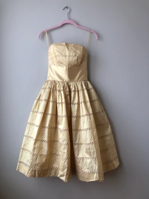 Vintage 50-tal Prom Dress - Axelbandslös klänning från 50-talet. Tjockare guld/gul siden med broderier, fodrad, zip bak. Insnitt + små veck vid byst för en lite strutigare form.  Midja: 62 cm,  Ryggbredd: 38,5 cm,  Kjollängd: 62 cm Skickar fler mått i dm till den intresserade.