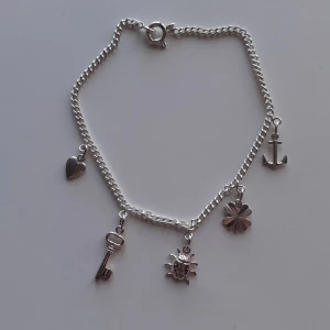 Silverarmband  - Armband i äkta silver med 4 söta berlocker i form av hjärta, nyckel, nyckelpiga, fyrklöver och ankare. 18 cm långt, nyskick och helt oanvänt.  Ask: 10 kr (valfritt) Frakt: 15 kr