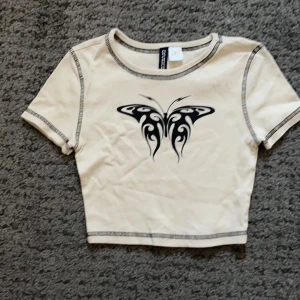 En croppd t-shirt med fjäril på  - Köpte tröjan på H&M för något år sedan och vill inte ha kvar den. Använd 2 gånger men har mest legat i garderoben. 