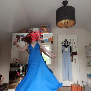 Balklänning blå - Balklänning från ca 70-80 tal, originellt från NK. Jag köpte den för 750 kr på en secondhandbutik, tycker den är jättefin och skön att ha på sig. Dock använde jag den aldrig, eftersom jag hittade en annan. Klänningen är väldigt "flowig", jag försökte visa det med andra bilden. Tyget är tungt, så det känns att det är ett lyxigt tyg. Jag (+klackarna) är 180 cm lång och klänningen hänger ~5 cm över marken. Klänningen är i perfekt skick vad jag kan se, broschen där fram går att ta av. 