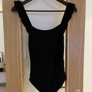 Svart ribbad body från Zara - Ribbad body från zara med djup rygg och volangband. Använd 1 gång så i jättefint skick. 