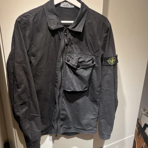 Stone Island - Garment Dyed Cotton Overshirt Svart - Säljer en svart Stone Island Overshirt i mycket bra skick! Inga frakturer på jackan över huvud taget då den knappt är använd! Kan lösa närbilder på patchen men även lösa en bild på QR-koden!  Säljer pågrund av att jag växt ur den! Strl: M