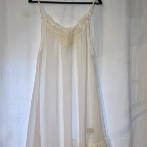 Klänning - Vit genomskinlig klänning med detaljer i urringningen. Osymmetrisk skärning nertill