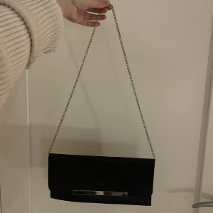 vintage väska - Vintage kuvert-väska men silvrig kedja!! Svart och glittrig och perfekt till fest eller andra event där man vill ha en simpel men lite extra snygg väska!!!