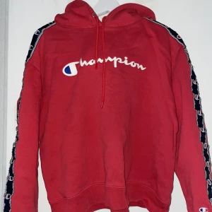 Champion hoodie - Röd champion hoodie med loggan längs ärmarna. Köpt från JD Sports men minns ej originalpriset. Skriv för mer bilder