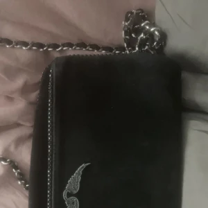 Zadig Väska - Zadig väskan är köpt för ca 1 år sen och är använd. Observera att vissa av väskans ”kristaller” fallit av. Väskan är köpt på Jackie för ca 4500kr och är svart och mocka material. Ni behöver swisha mig först o kommer såklart skicka bevis på paketet innan
