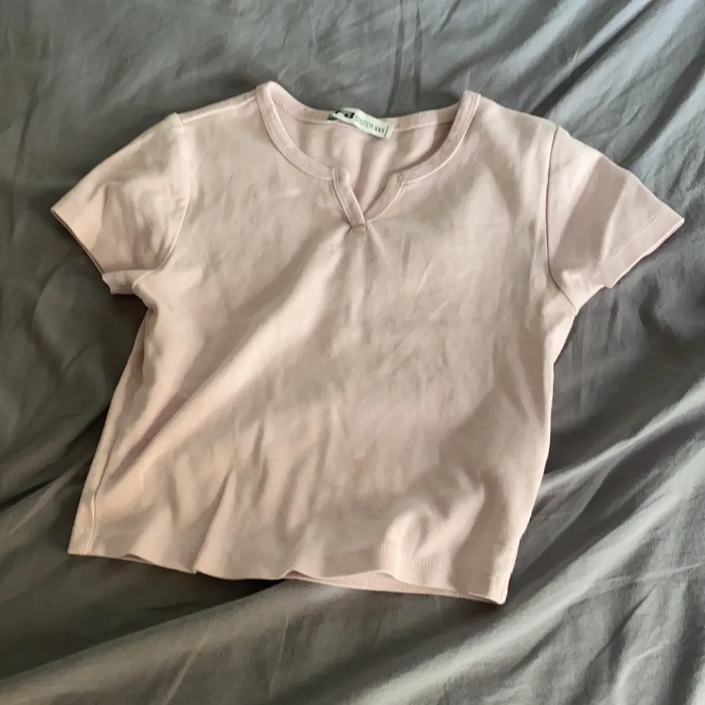 Säljer denna T-shirten i färgen rosa med en liten slint där uppe. T-shirts.