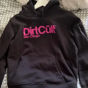 En svart dirtcült hoodie med rosa text i storlek XL men den passar mig som har S, så skulle säga att den är väldigt liten i storlek🩷
