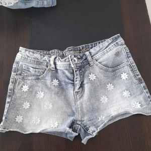 Shorts  - Low waist jeans shorts med blommor.köpta för 3 år sedan i Usa.Använda runt 10 gånger men är i bra skick.Storlek runt 12-14 år ( runt midja 66 cm, längd 25 cm .❤