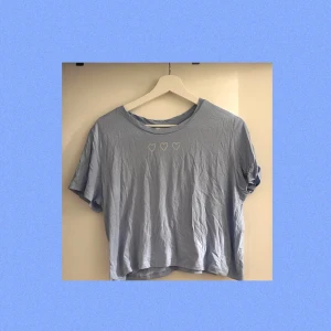 💙Blå t-shirt med hjärtan💙 - En söt, blå t-shirt raka vägen från Monki! Tröjan har tre små hjärtan som går över bröstet. Modellen är lite kortare och slutar strax vid naveln. Köparen står för frakt😘
