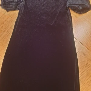 Festklänning - Nästan oanvänd klänning i sammet/velour med "frasiga" puffärmar i genombrutet tyg. 85 cm lång från nacke till nederkant, ungefär knälång. Lite stretchig i tyget.