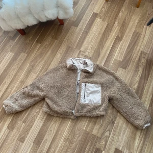 Jacka - En jacka som kan användas åt båda hållen. Ena hållet som en teddyjacka och andra som en bomberjacka med lurvet på insidan. Lappen är borttagen då jag fått den i present, men jackan har aldrig kommit till användning. Priset är diskuterbart.