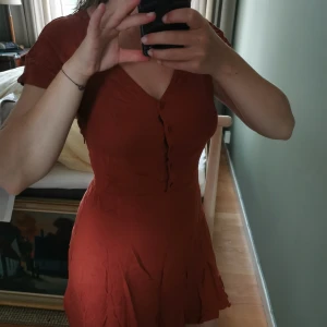 Klänning - Roströd/orange klänning från weekday, v-ringad med knappar fram. Jättefin men inte riktigt min stil och därav aldrig använd 