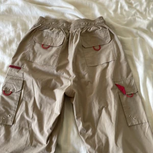 Cargo byxor - Säljer ett par cargo byxor i färgerna beige och rött. Dom har en justerbar midja dom har flera fickor på både fram och baksidan. Dom är köpta från secondhand men är i jätte bra skick!