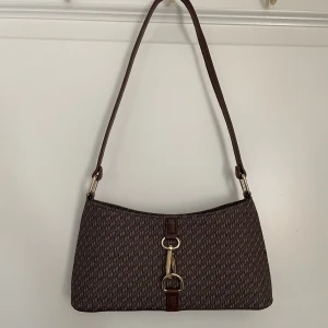 Handväska Y2k 90-talsstil  - Jättefin populär handväska / axelremsväska från ASOS. Den är HEL NY. Missade returnera den i tid, har en liknande redan🤎 Monogram mönstrad brun färg med guld metallspänne.  Den är slutsåld på ASOS. Skickas Spårbart💜