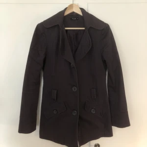 Jacka - Mörklila trenchcoat som passar perfekt till våren. Den är inte lång utom slutar under magen liksom.
