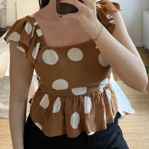 Brun blus med vita prickar - Brun blus med vita prickar och volanger. Knytning i rygg