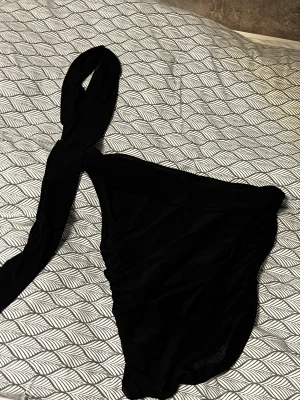 Svart oneshoulder festtopp - Säljer en svart oneshoulder topp med lång ärm på ena sidan. Toppen är croppad och har en tight passform som framhäver siluetten. Materialet känns mjukt och stretchigt, 