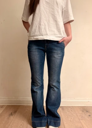 Blå bootcut jeans med broderade fickor - Innerbenslängd: 80 cm                               Midjemått rakt över: 37 cm                          Grenlängd: 15 cm                                   Benöppning: 25 cm