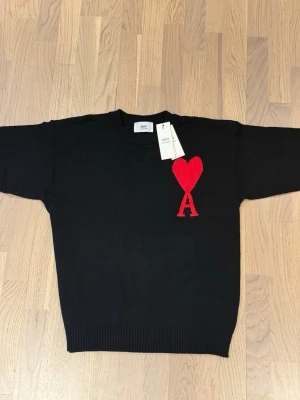 Svart stickad tröja från Ami - Svart stickad tröja från Ami Alexandre Mattiussi med rund hals och ribbade muddar. På bröstet finns ett stort rött hjärta med bokstaven A. Tröjan har lång ärm och är gjord i mjuk bummul säljer den för att den inte passar mig då den va lite för liten