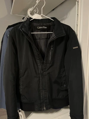 Svart jacka från Calvin Klein - Svart jacka från Calvin Klein. Säljer då den är för liten för mig! Det saknas en knapp på vardera ficka på utsidan. Jackan har även två innerfickor. Storlek XS.