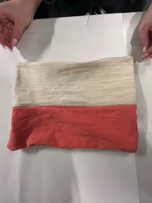 Beige och röd datorväska i bomull - Säljer en stilren datorväska i tvåfärgad design med beige ovandel och röd underdel. Väskan är tillverkad i mjuk bomull och har en enkel, rektangulär form. 