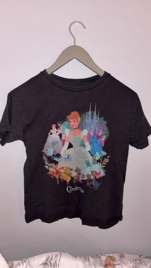 Svart Cinderella t-shirt Pull&Bear  - Svart t-shirt från Pull&Bear x Disney Princess med  Cinderella-tryck framtill. Perfekt för dig som älskar Disney eller känner någon som gör det. Kan användas vardagligt eller som pyjamas.   ÄR EN XS MEN ÄR STOR I STORLEK